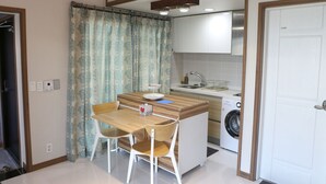 A compact kitchen with a wooden table and chairs, a washing machine, and a sink. - Daisy (Jeju City)