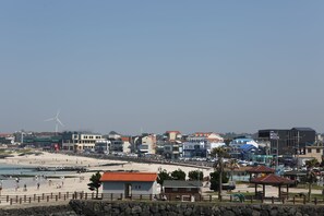 A coastal town with a beach, buildings, and a wind turbine. - Dahlia (Jeju City)