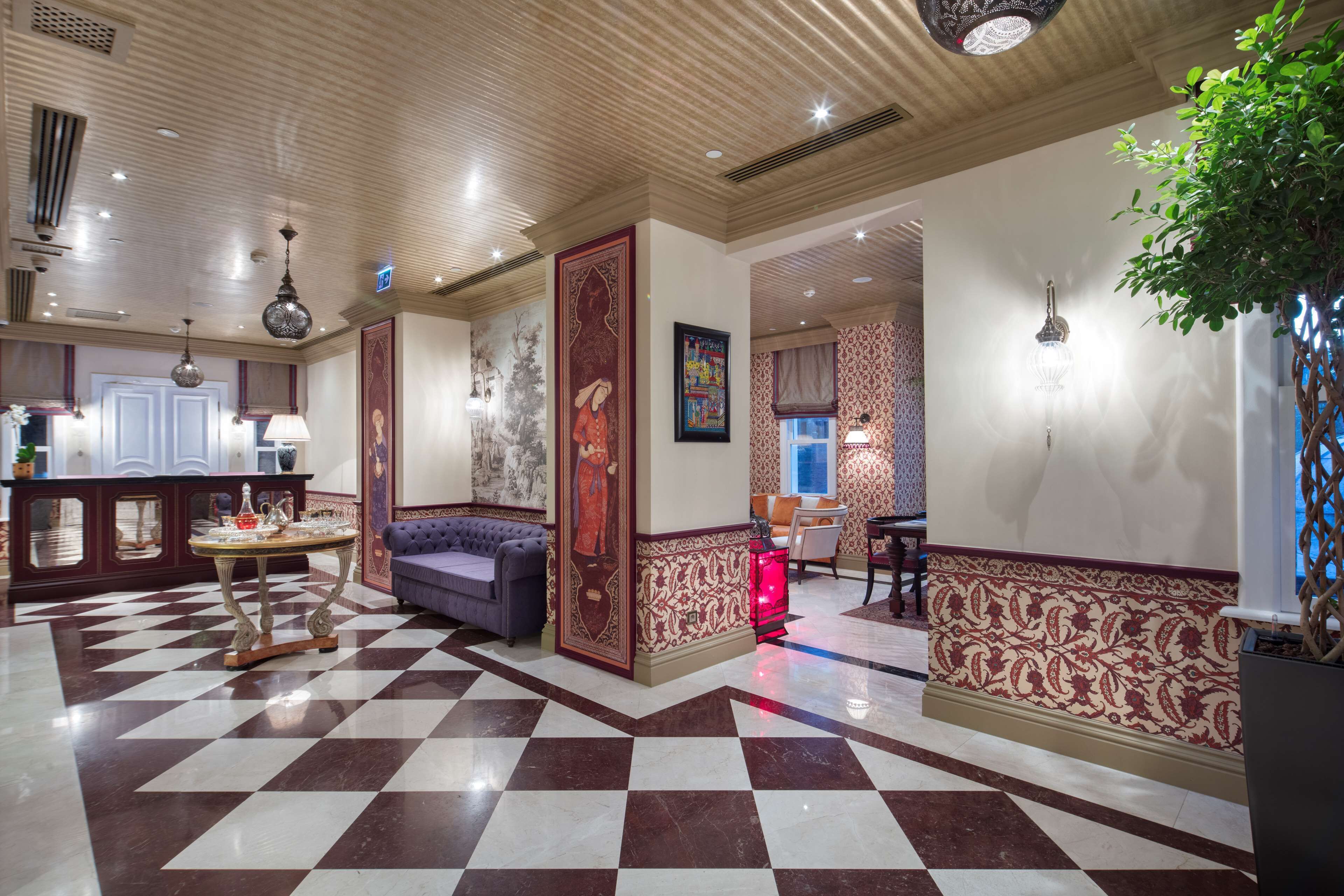 Un vestíbulo de hotel con piso a cuadros, un sofá, una mesa con adornos y una planta grande.