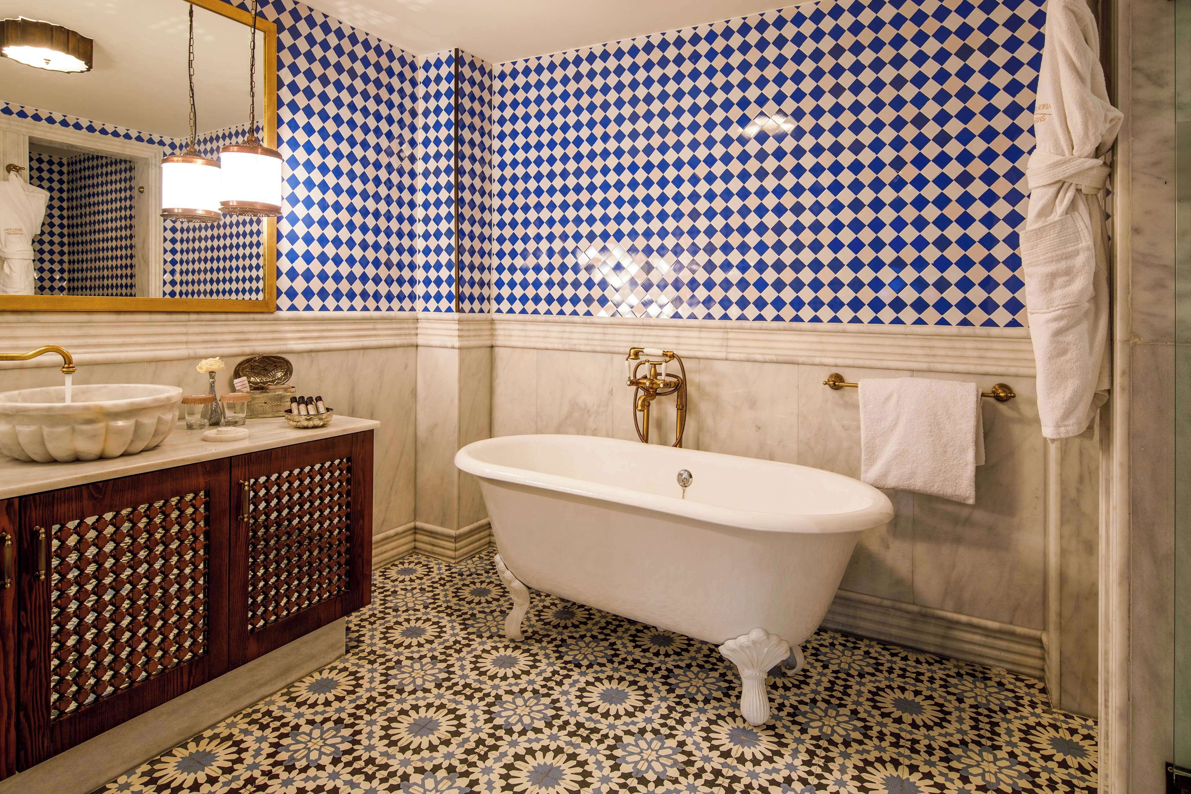 A bathroom with a freestanding bathtub, a large mirror, and a patterned floor.