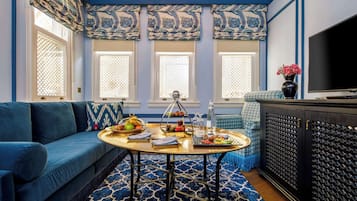 Una habitación con un sofá azul, una mesa redonda de centro con una bandeja de comida, un televisor y un mueble decorativo.