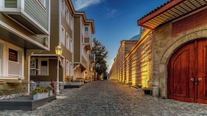 A cobblestone street lined with historic buildings, featuring a prominent red wooden door and a row of lit windows.