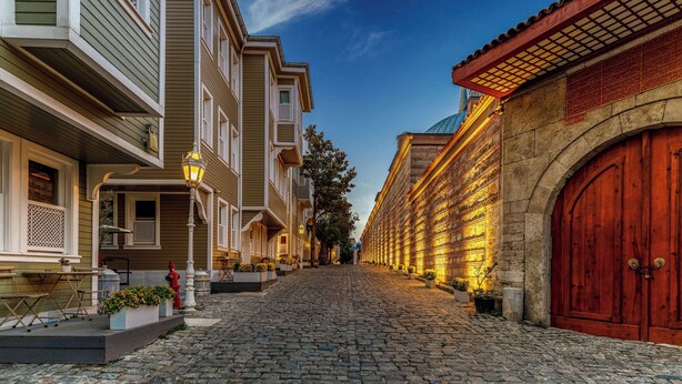 A cobblestone street lined with historic buildings, featuring a prominent red wooden door and a row of lit windows. - Hagia Sofia Mansions Istanbul, Curio Collection by Hilton (Istanbul)