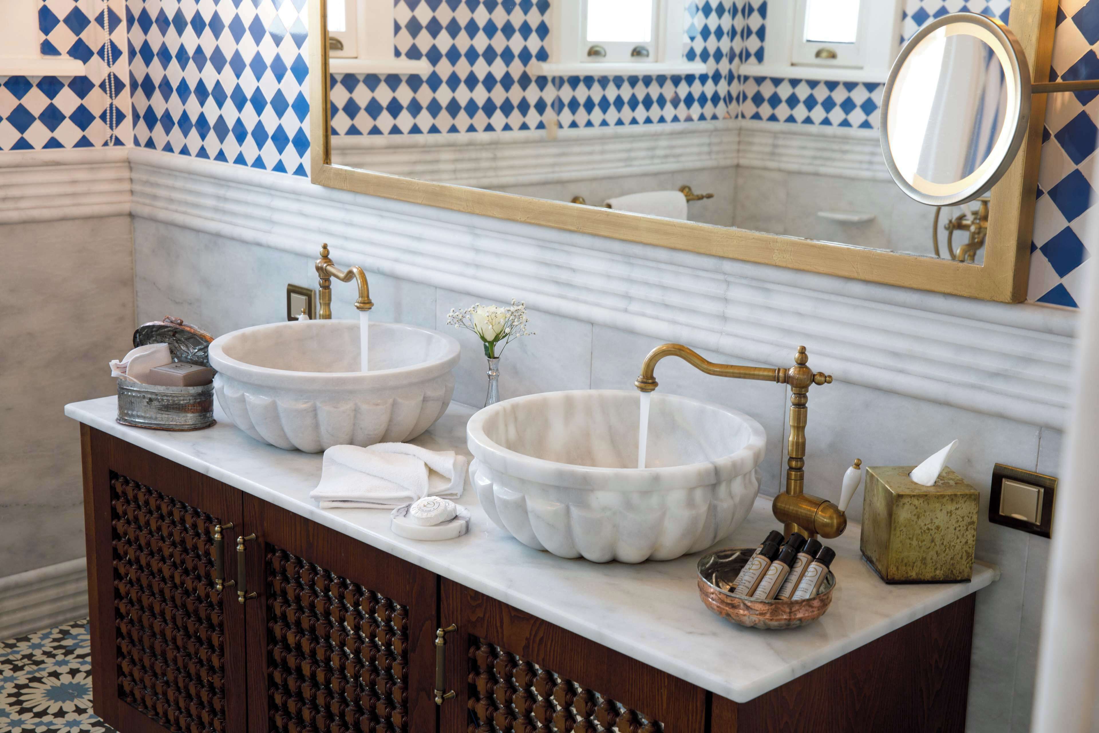 A bathroom with two marble sinks, a wooden cabinet, a mirror, and a patterned tile backsplash.