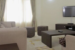 A living room with a sofa, ottomans, a coffee table, and a flat-screen TV mounted on the wall. - Perfect Havens at Noah's Court (Lekki)