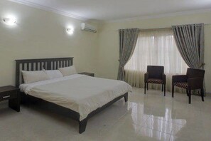 A bedroom with a bed, two chairs, a nightstand, and a window with curtains. - Perfect Havens at Noah's Court (Lekki)