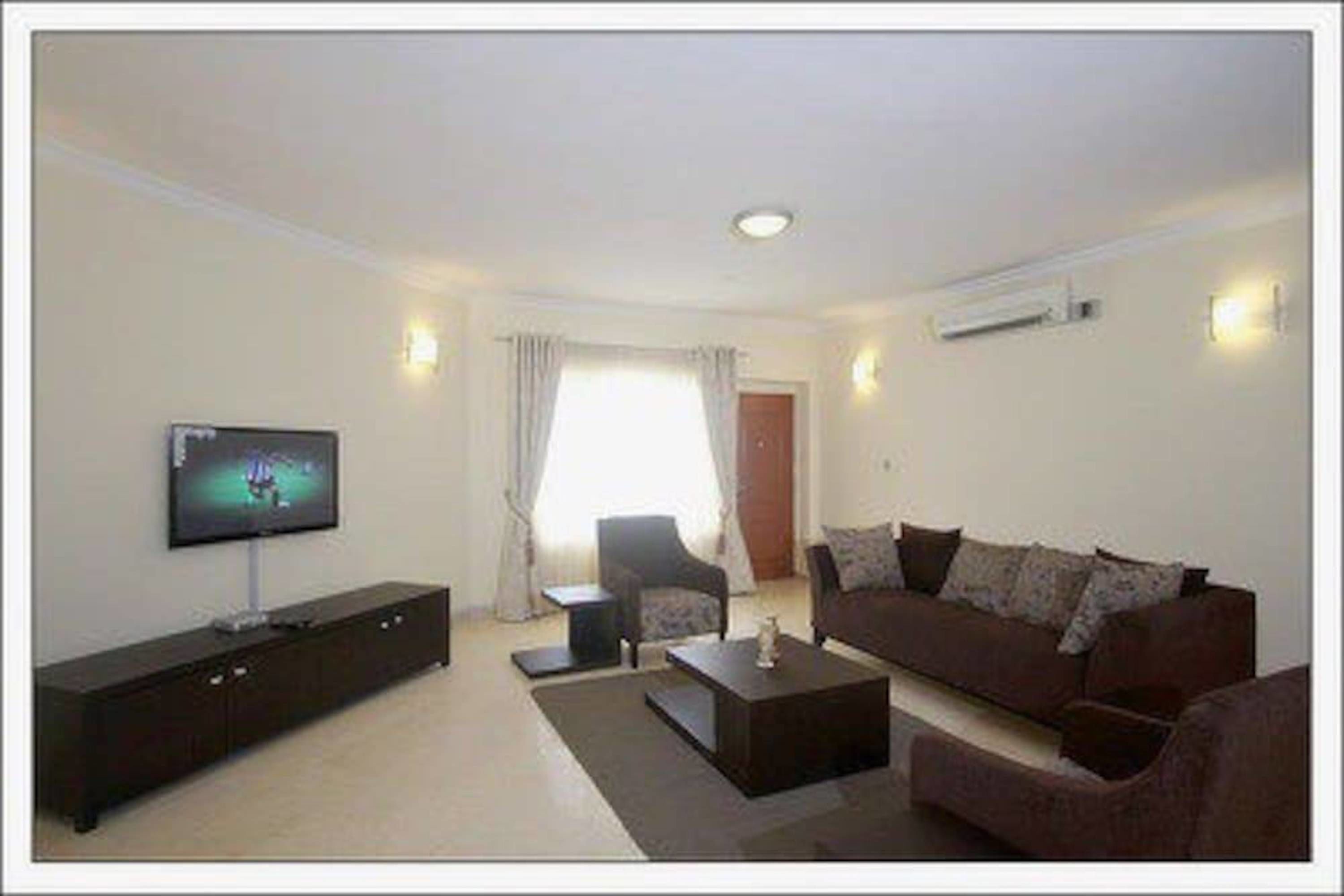 A living room with a flat-screen TV, a dark brown sofa, a coffee table, and a dark brown cabinet.