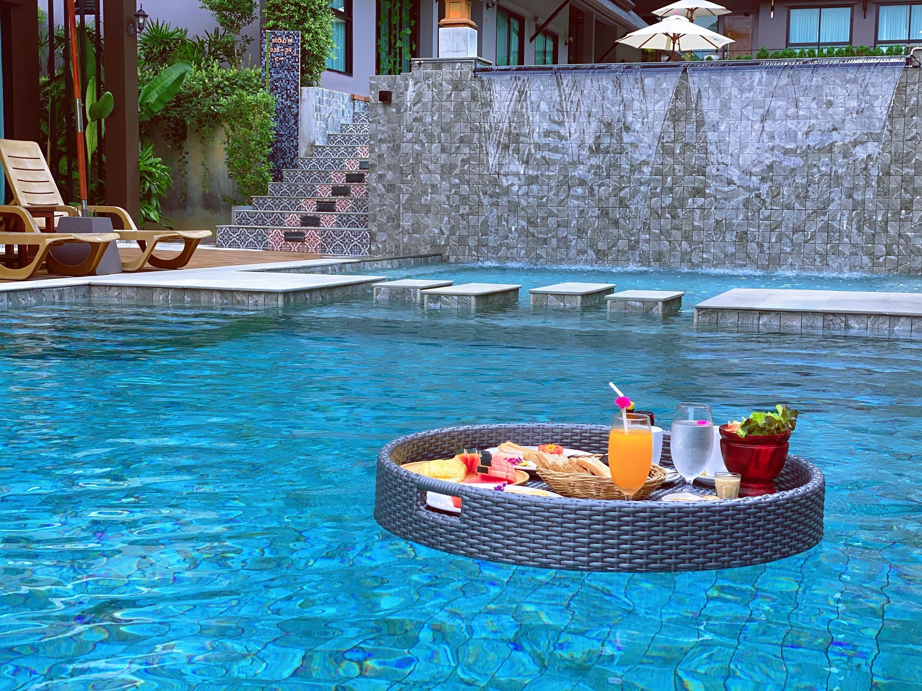 A pool area with a floating bar, lounge chairs, and a stone wall.