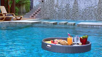 Zona de piscina con un bar flotante, sillones de descanso y una pared de piedra.