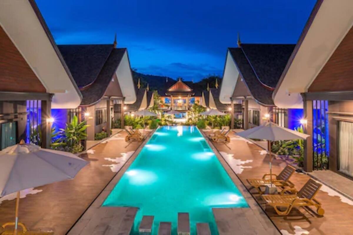 A swimming pool with lounge chairs and umbrellas, surrounded by buildings with traditional architecture.
