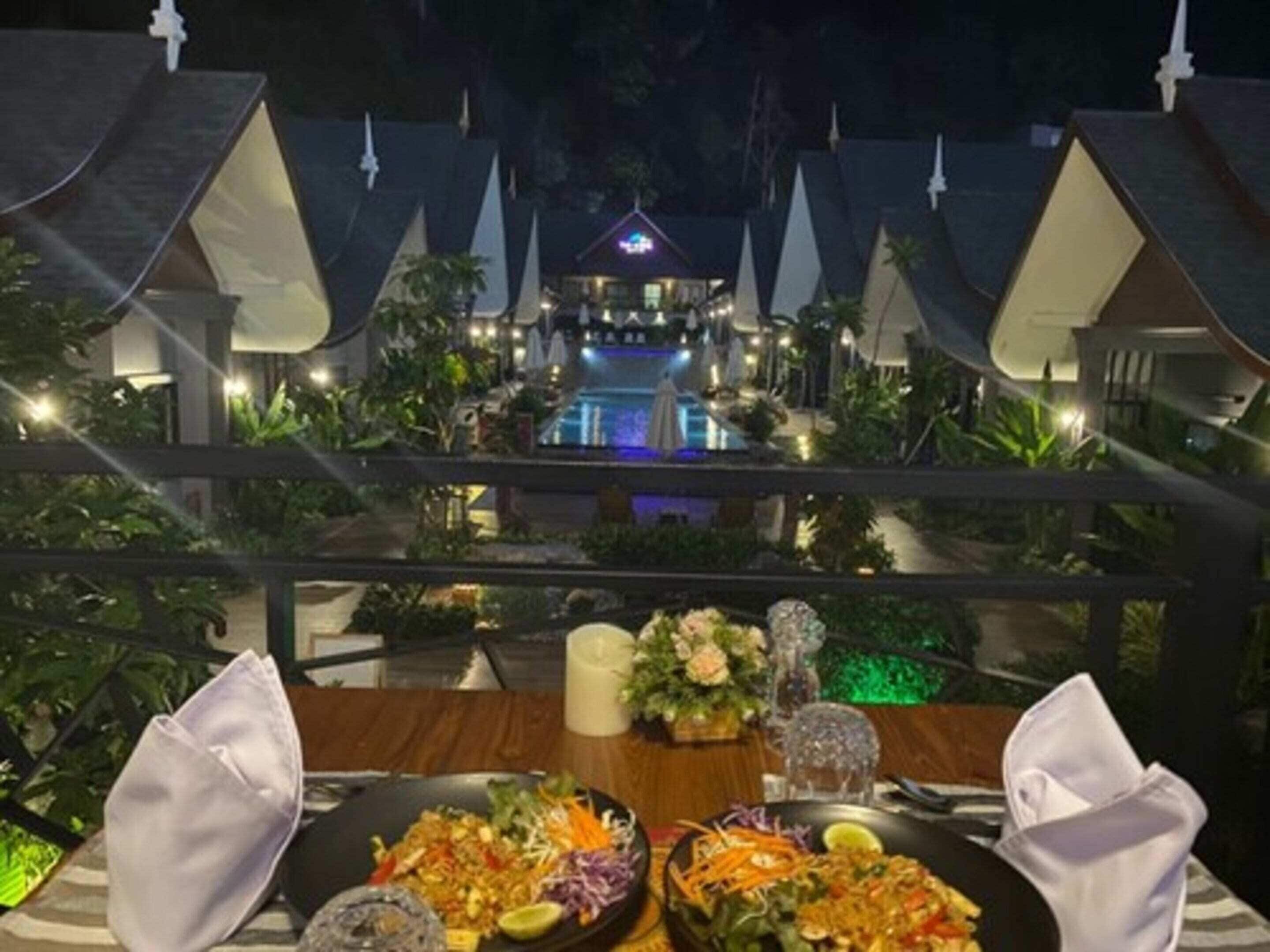 Een eettafel met een maaltijd en uitzicht op een resort met meerdere gebouwen en een zwembad.
