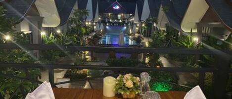 Una mesa de comedor con comida y vistas a un resort con varias edificaciones y una piscina.