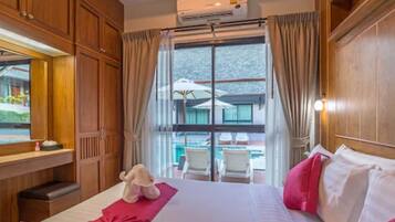 A hotel room with a large bed, wooden furniture, a view of a pool, and an air conditioning unit.