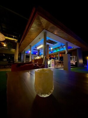 An indoor setting with a wooden table and a glass of a yellow beverage. There is a seating area with a red couch and a person in the background. - The Scene Cliff View Villas (Krabi)