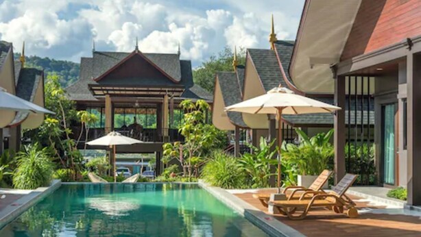 A pool area with lounge chairs and umbrellas, surrounded by lush greenery and traditional architecture. - The Scene Cliff View Villas (Krabi)