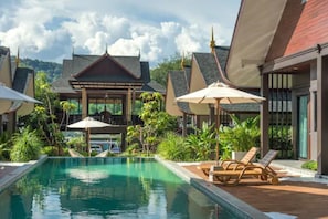 Área de piscina com espreguiçadeiras e guarda-sóis, cercada por vegetação exuberante e arquitetura tradicional.