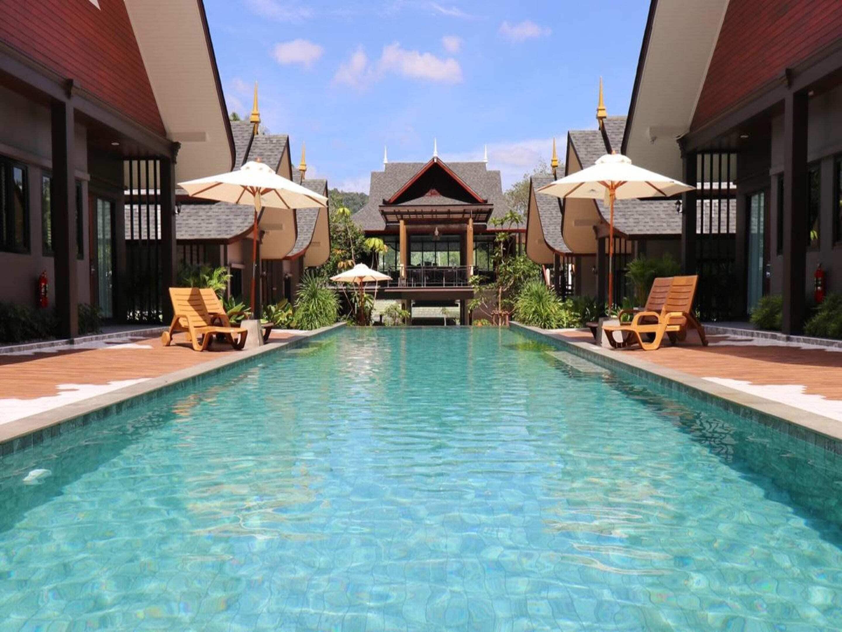 Ein Swimmingpool mit Liegestühlen und Sonnenschirmen, umgeben von Gebäuden mit traditioneller Architektur.