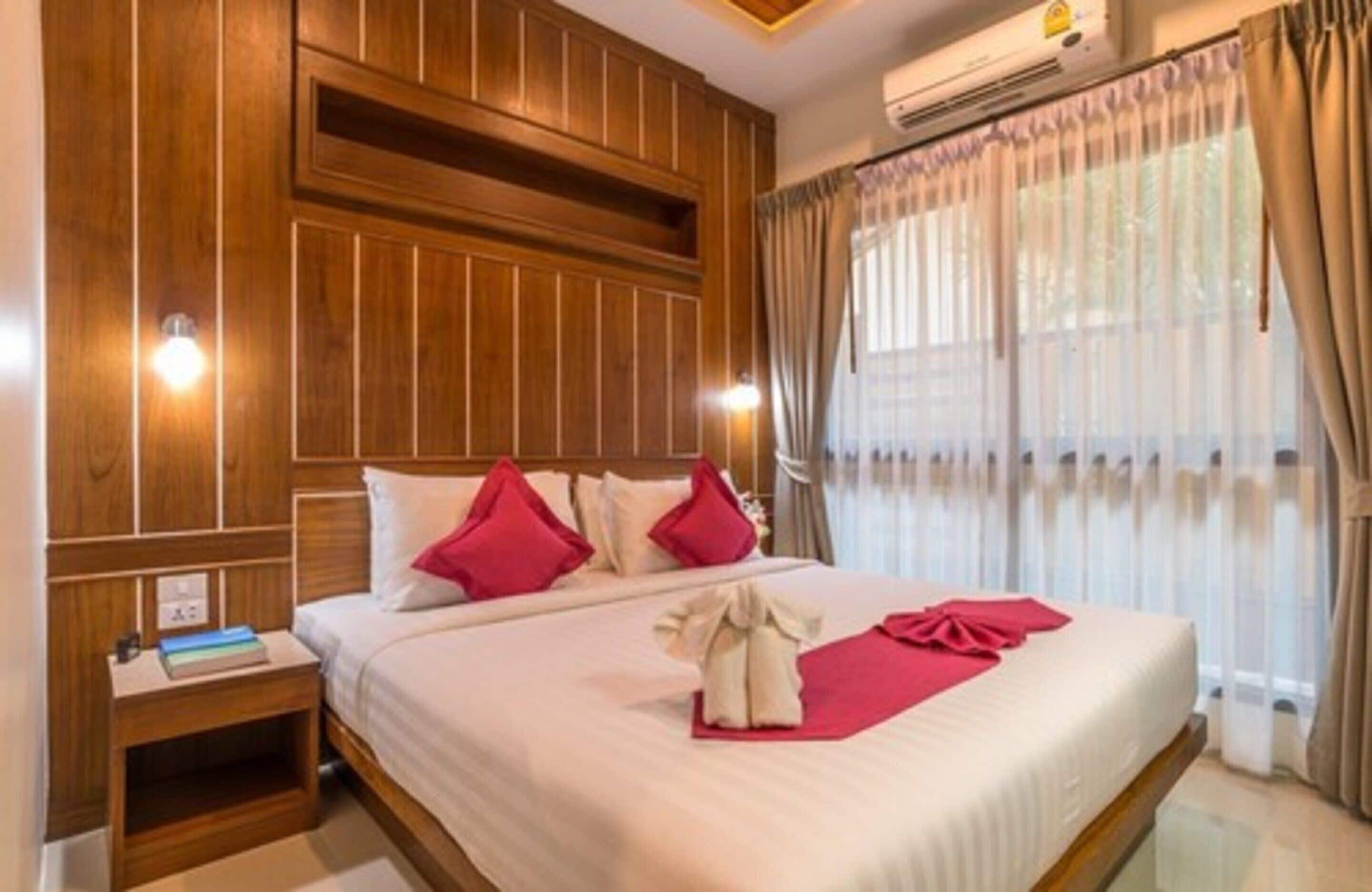 A hotel room with a large bed, wooden paneling on the walls, a nightstand with a book, and a window with curtains.
