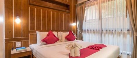 A hotel room with a large bed, wooden paneling on the walls, a nightstand with a book, and a window with curtains.