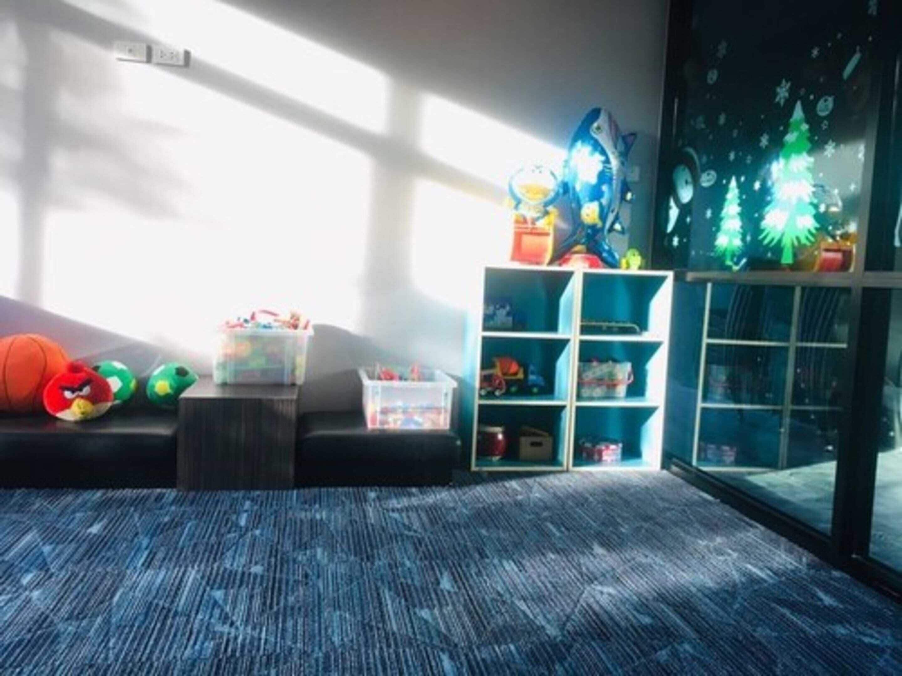A room with a window, a blue carpet, a bookshelf, and a toy shelf.