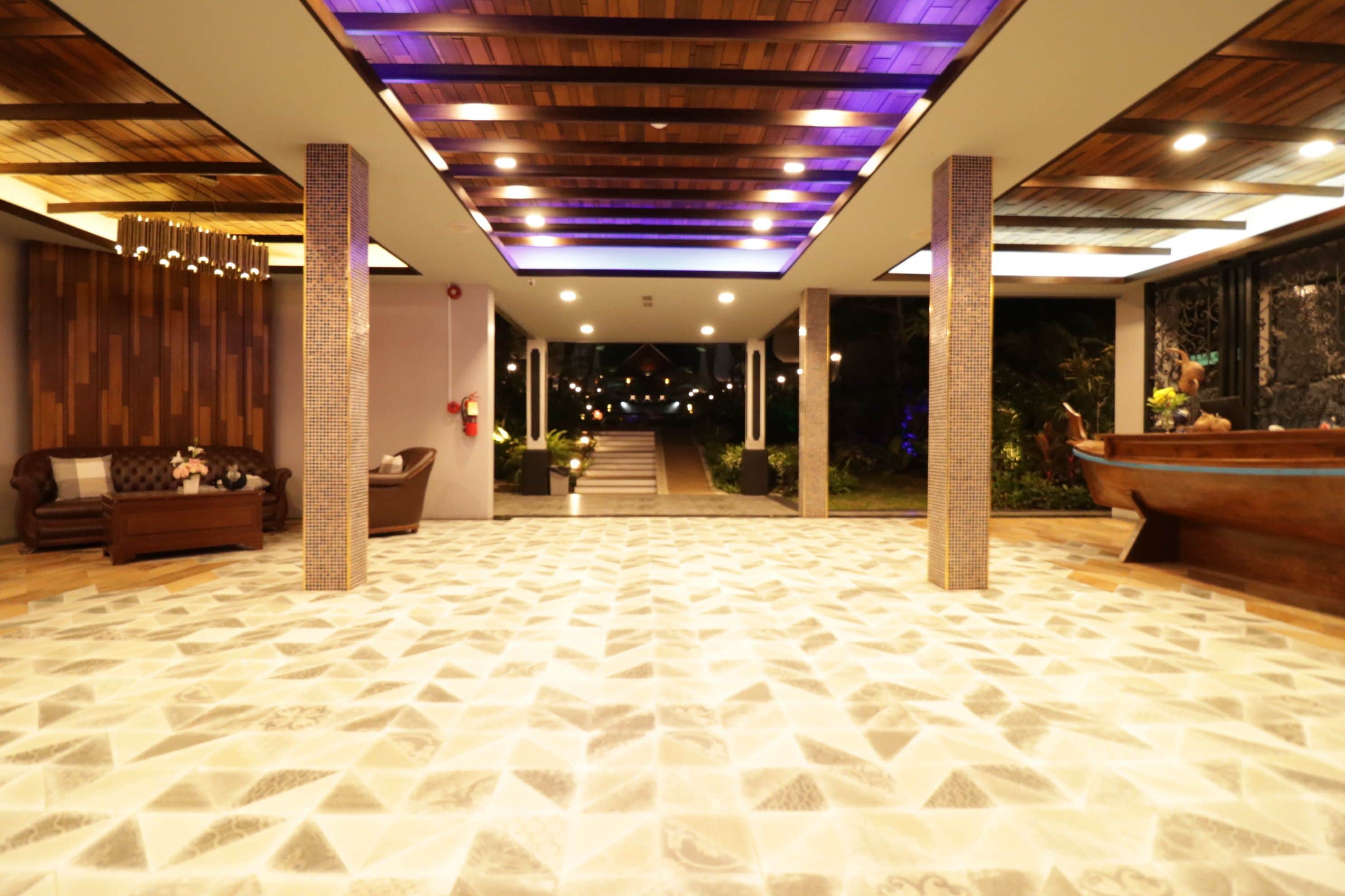 A spacious lobby with a patterned floor, wooden ceiling, and a reception area with a large aquarium.