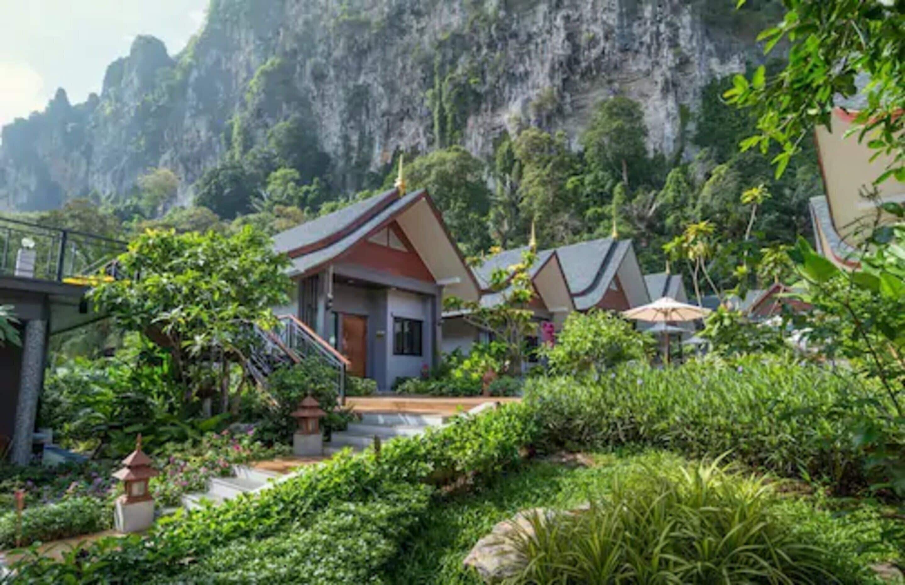 A traditional Thai-style building with a steeply pitched roof, surrounded by lush greenery and a mountainous backdrop.