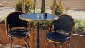 Two wicker chairs with a round table, placed outdoors with a view of buildings and trees in the background. - Hotel Le Relais Du Postillon (Antibes)