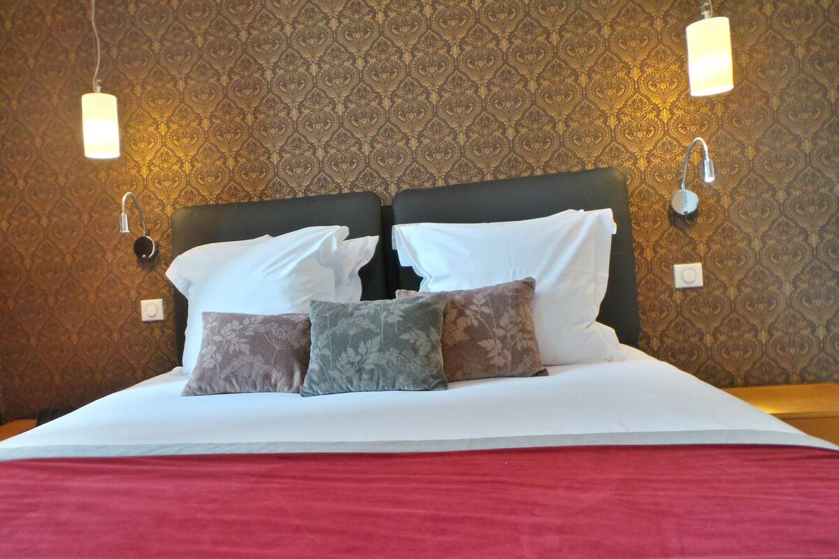 A neatly made bed with white linens and multiple pillows, set against a patterned wallpaper.