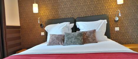 A neatly made bed with white linens and multiple pillows, set against a patterned wallpaper.