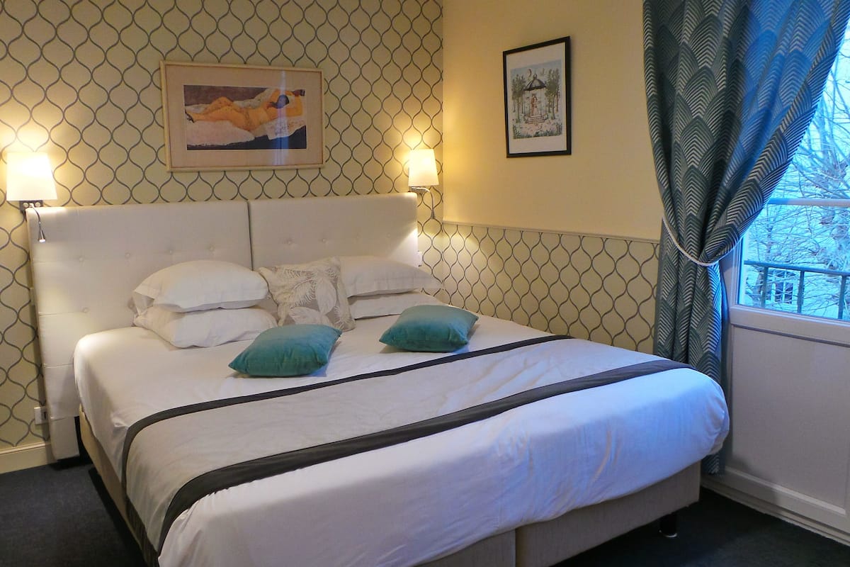 A neatly made bed with white bedding and two teal pillows, a headboard with a geometric pattern, and two framed pictures on the wall.