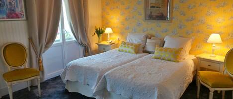 A hotel room with a double bed, two bedside tables with lamps, a chair, and a window with curtains.