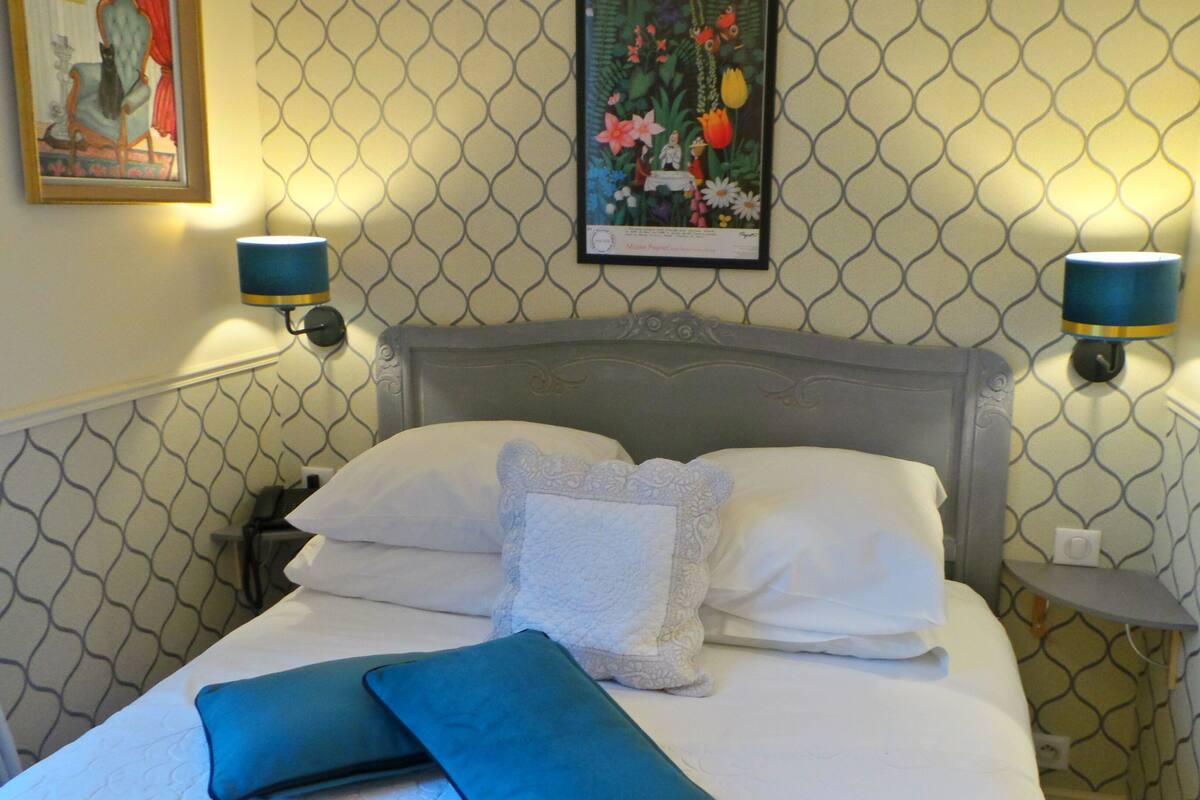 A neatly made bed with white linens and a decorative pillow, two wall-mounted lamps, and a framed floral artwork above the bed.