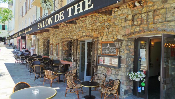A stone building with a sign reading "SALON DE THE" and outdoor seating with wicker chairs and round tables. - Hotel Le Relais Du Postillon (Antibes)
