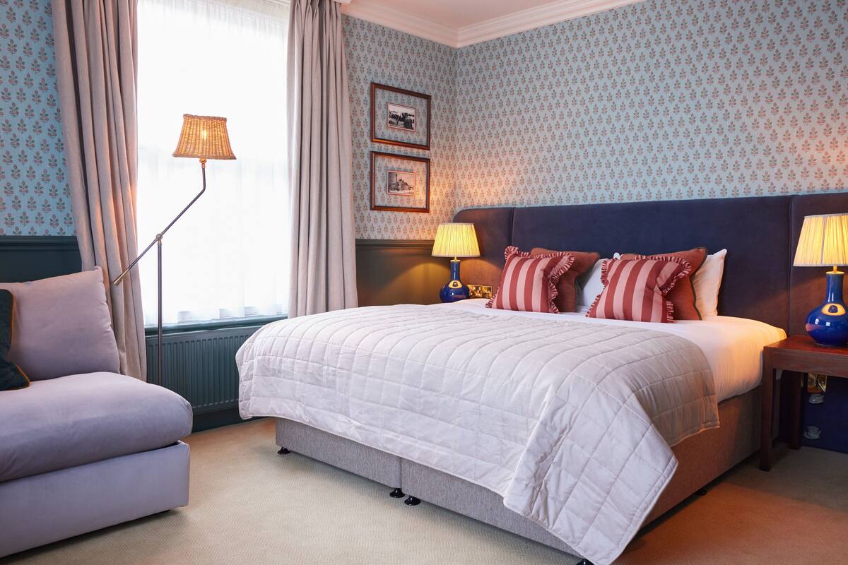 Een keurig opgemaakt slaapkamer met een groot bed, een nachtkastje, een lamp en een stoel.