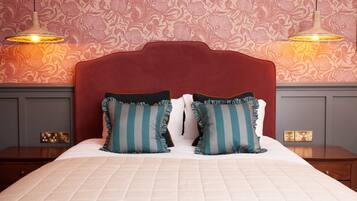 A hotel room with a large bed, two bedside tables, a red headboard, and patterned wallpaper.