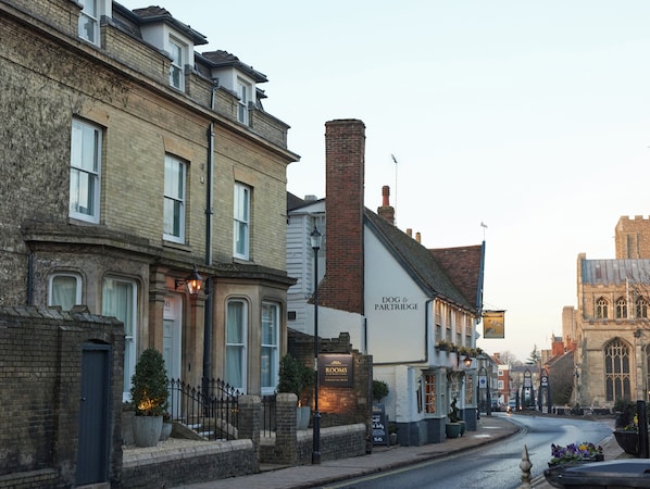 A street view with a pub named "Dog & Partridge" and a church in the background. - The Dog & Partridge by Greene King Inns (Bury St Edmunds)