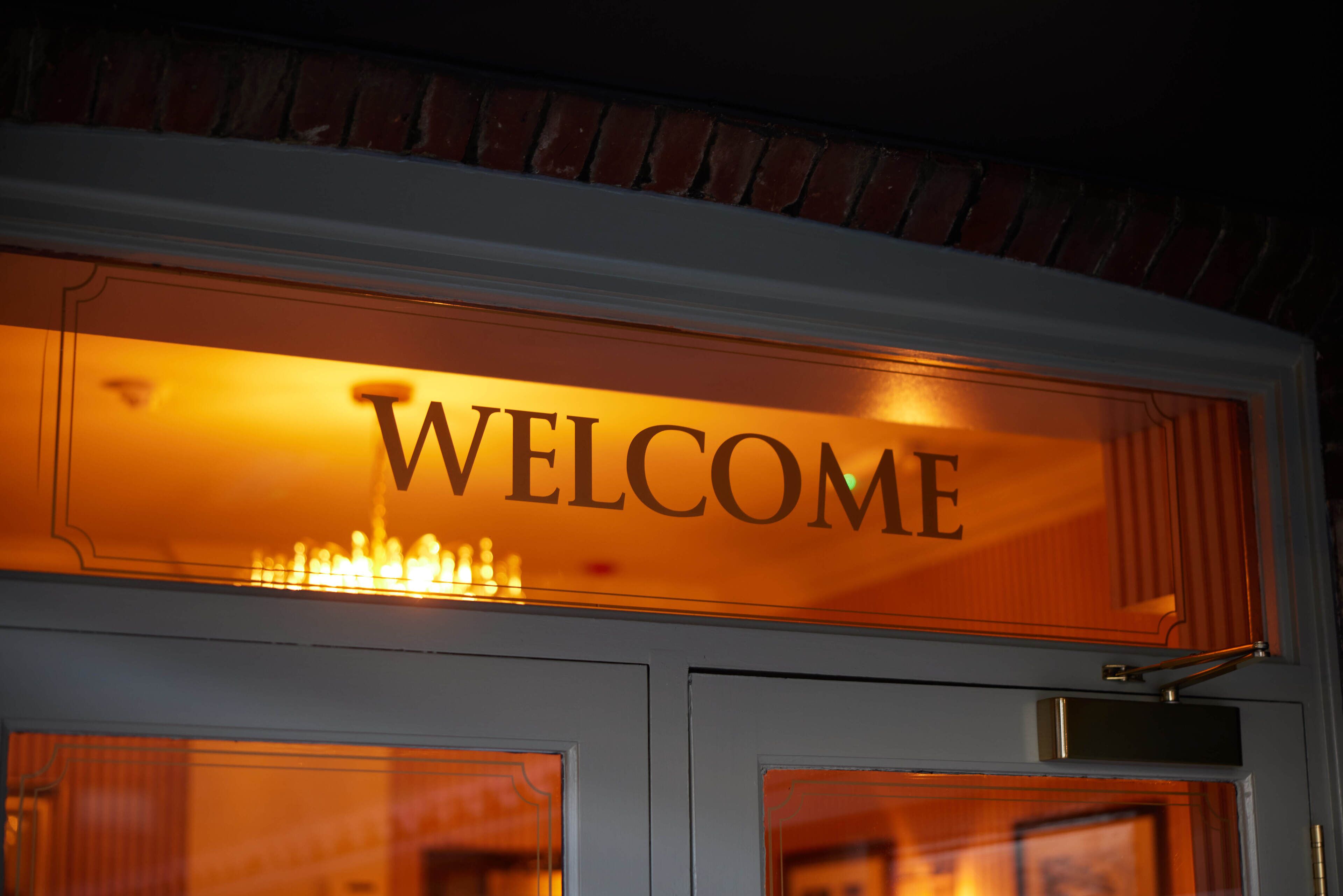 A "WELCOME" sign above a door with a brick wall and a white door frame.