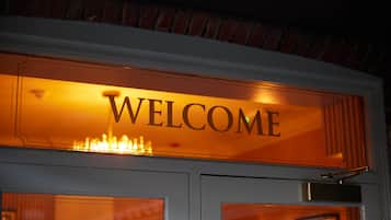 A "WELCOME" sign above a door with a brick wall and a white door frame.