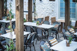 An outdoor café with tables and chairs, surrounded by a stone wall and wooden posts. - The Dog & Partridge by Greene King Inns (Bury St Edmunds)