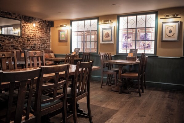 A restaurant interior with wooden tables and chairs, stone walls, and framed pictures on the walls. - The Dog & Partridge by Greene King Inns (Bury St Edmunds)