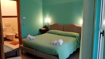 Une chambre d’hôtel avec un lit, une table de chevet, une lampe et une salle de bain visible à travers une porte ouverte.