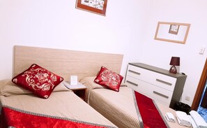Habitación de hotel con dos camas, una mesita de noche, una lámpara y un pequeño escritorio con otra lámpara.