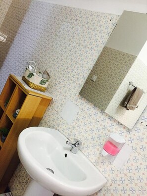 Un baño con lavamanos blanco, mueble de madera, baldosas de suelo estampadas y un espejo con una toalla colgada.