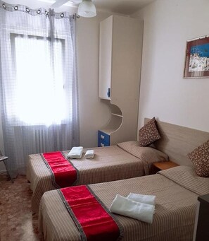 Habitación de hotel con dos camas, un armario, un escritorio y una ventana con cortinas.