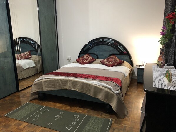 Un dormitorio ordenado con cama, mesita de noche, espejo y un jarrón decorativo.