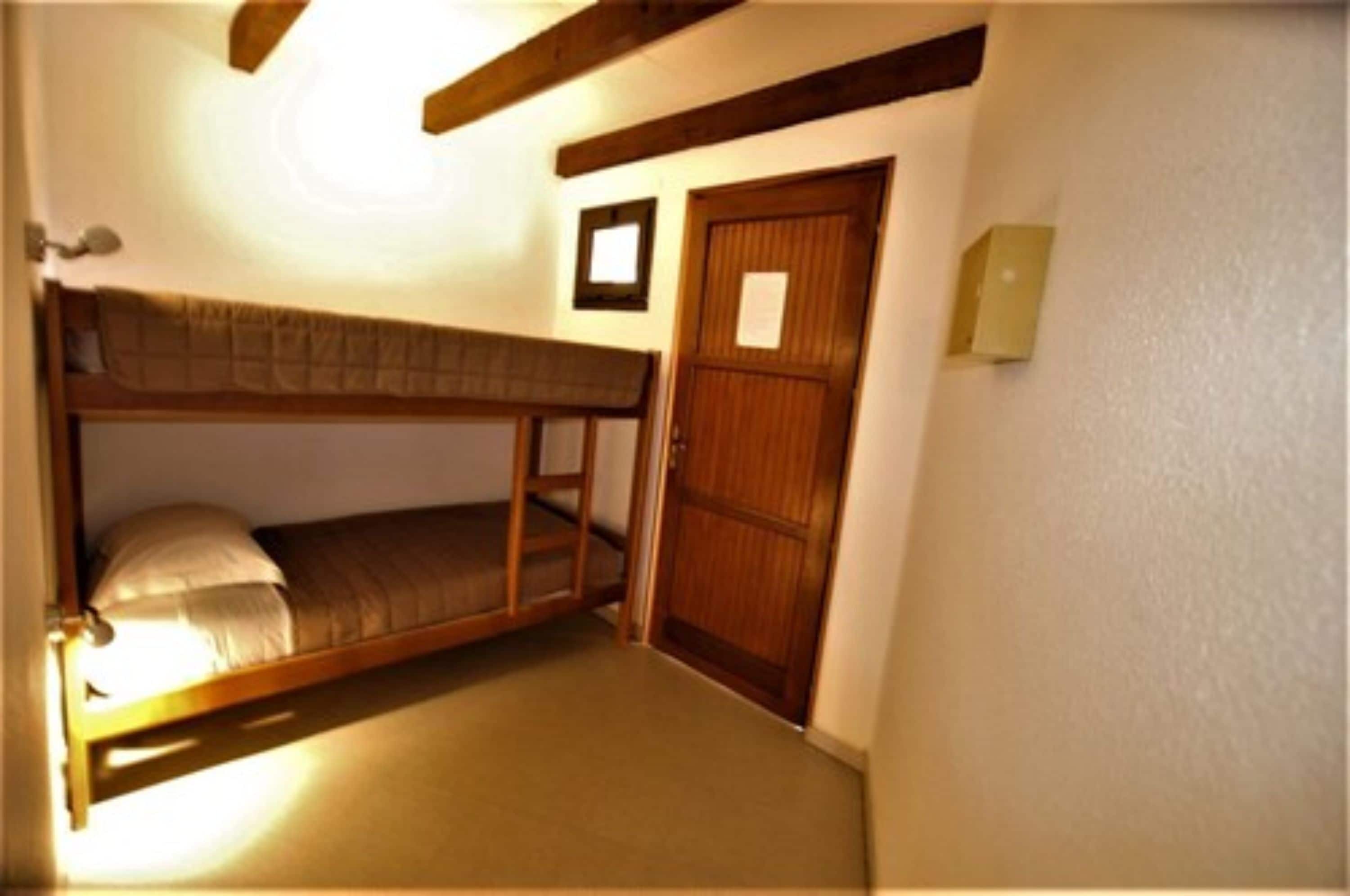 Una habitación pequeña con cama individual y literas de madera, una puerta de madera y un interruptor de luz en la pared.