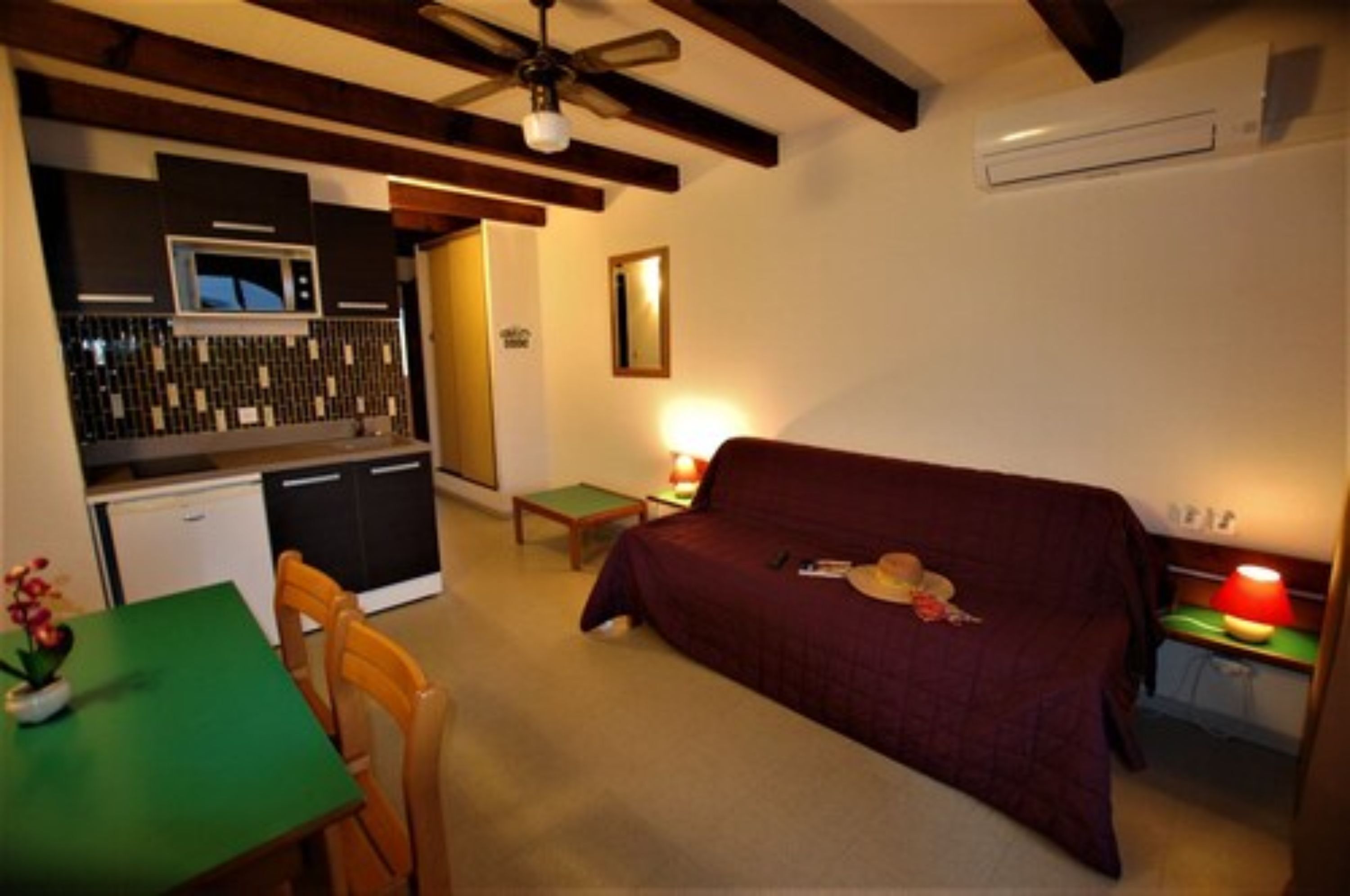 Una habitación compacta con kitchenette, cama, mesa de comedor y ventilador de techo.