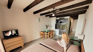 A bedroom with a bed, a TV on a dresser, a dining table with chairs, and a kitchen in the background. - Le California Motel (Vico)