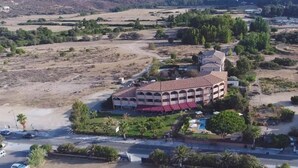 An aerial view of a building with a central courtyard, surrounded by greenery and a few parked cars. - Le California Motel (Vico)