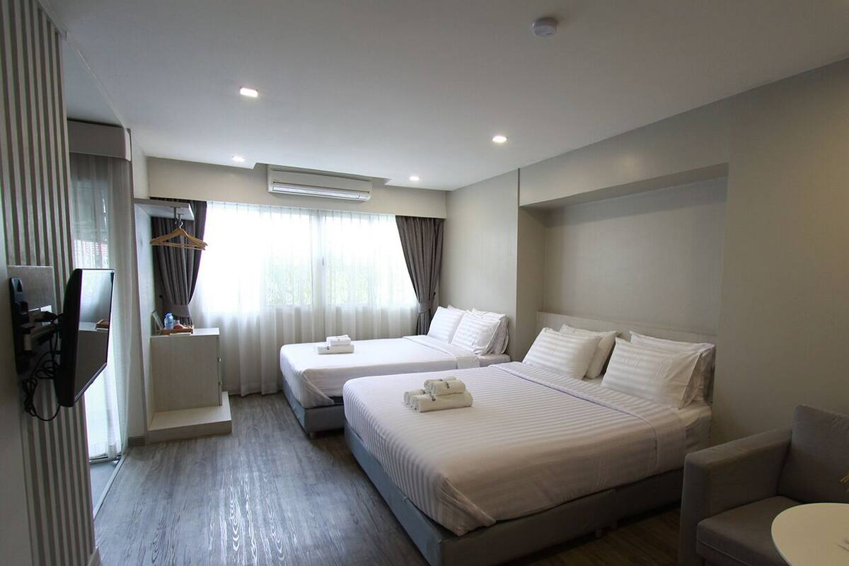 Camera d'albergo con due letti, televisore, scrivania e finestra con tende.